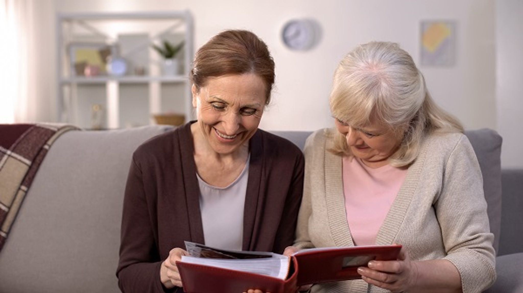 Two women on a sofa looking at old photographs in a photo album together to remember their deceased loved one