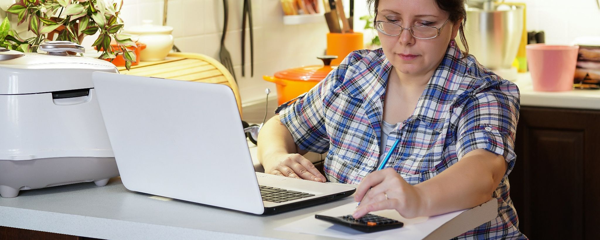 Lady Using Calculator In Kitchen