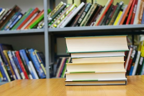 Library Books On Table In Front Of Shelf