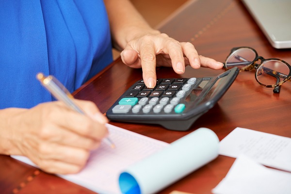 Woman working out expenses using a calculator, pen and paper with glasses