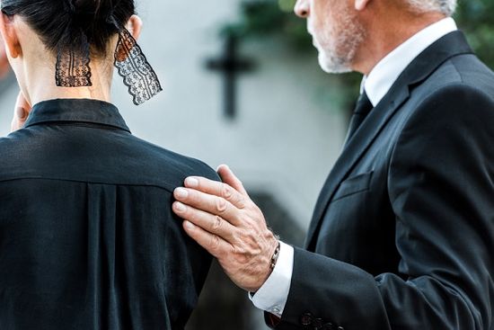 Man comforting woman with hand on shoulder during funeral