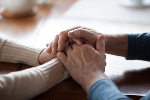 Close up of middle-aged people holding hands to comfort one another after the loss of a loved one