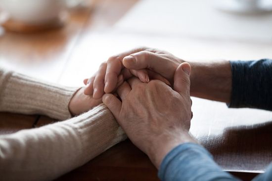 Close up of middle-aged people holding hands to comfort one another after the loss of a loved one