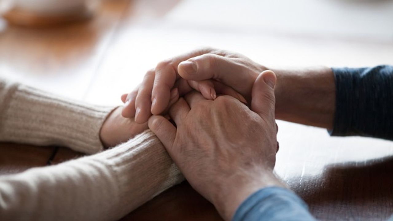 Close up of middle-aged people holding hands to comfort one another after the loss of a loved one